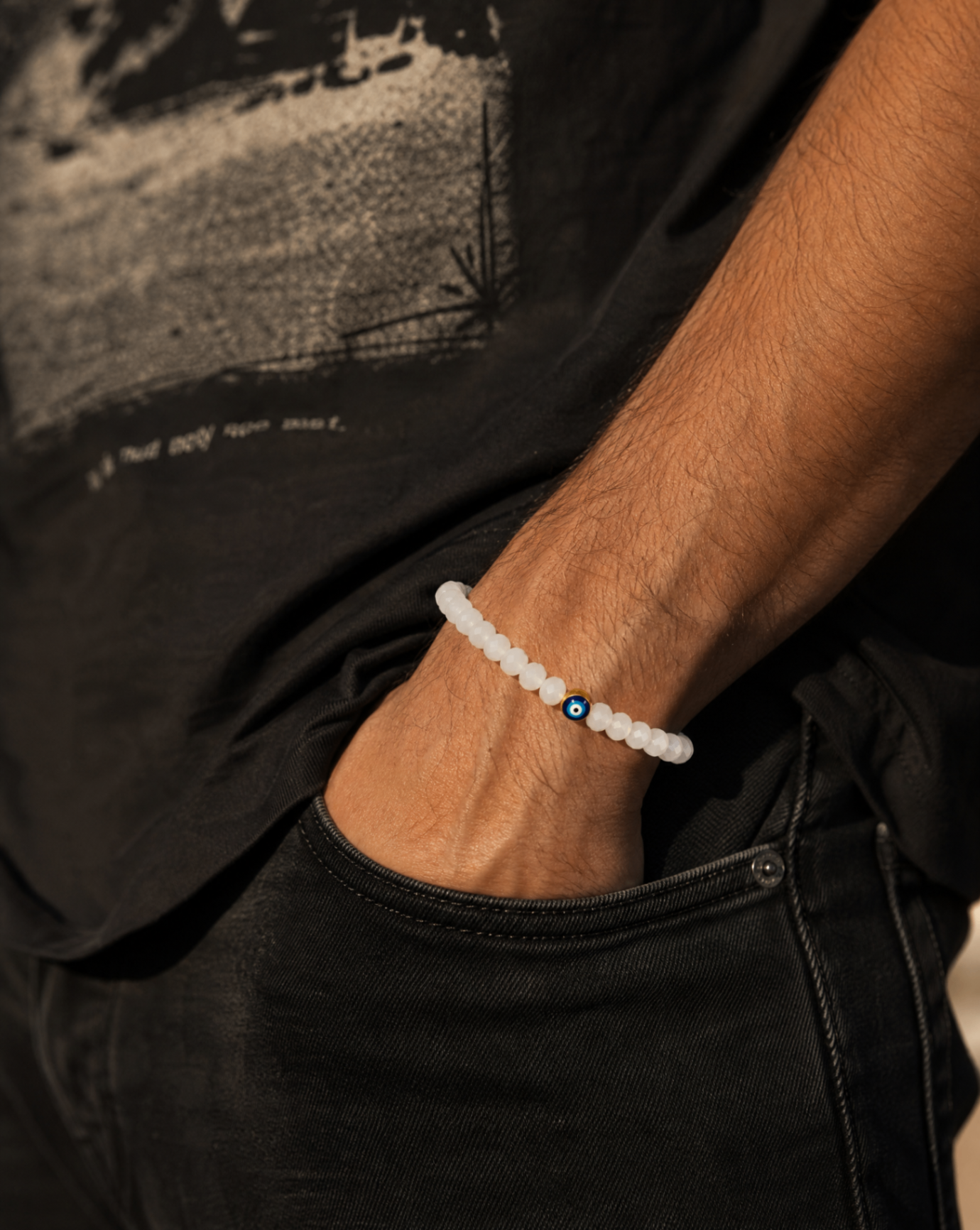 White beaded bracelet on a man's wrist resting in a black denim pocket