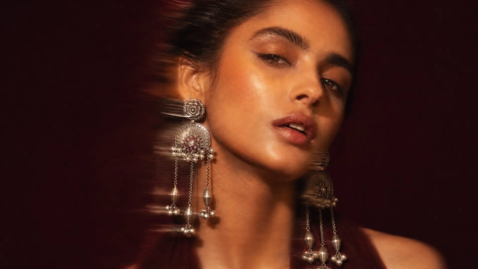 Model wearing silver chandbali chandelier earrings against a deep maroon backdrop