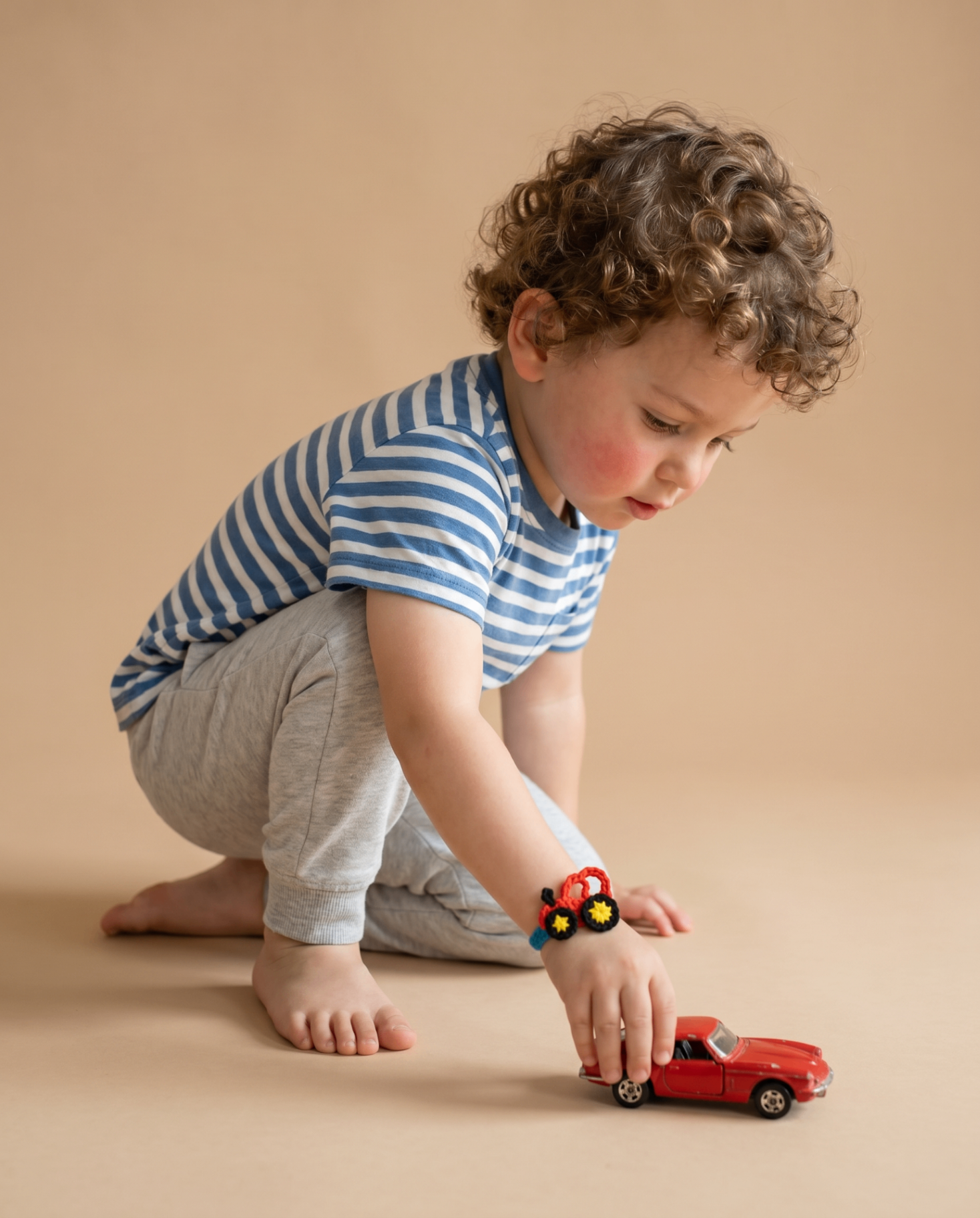 Young boy playing with a toy car while wearing a handmade rakhi bracelet