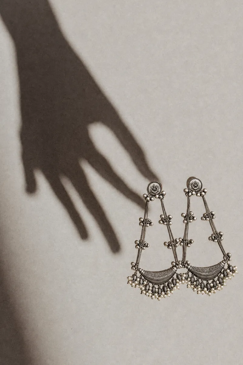 Handpicked oxidised silver chandbali earrings with pearl drops beside a soft hand shadow
